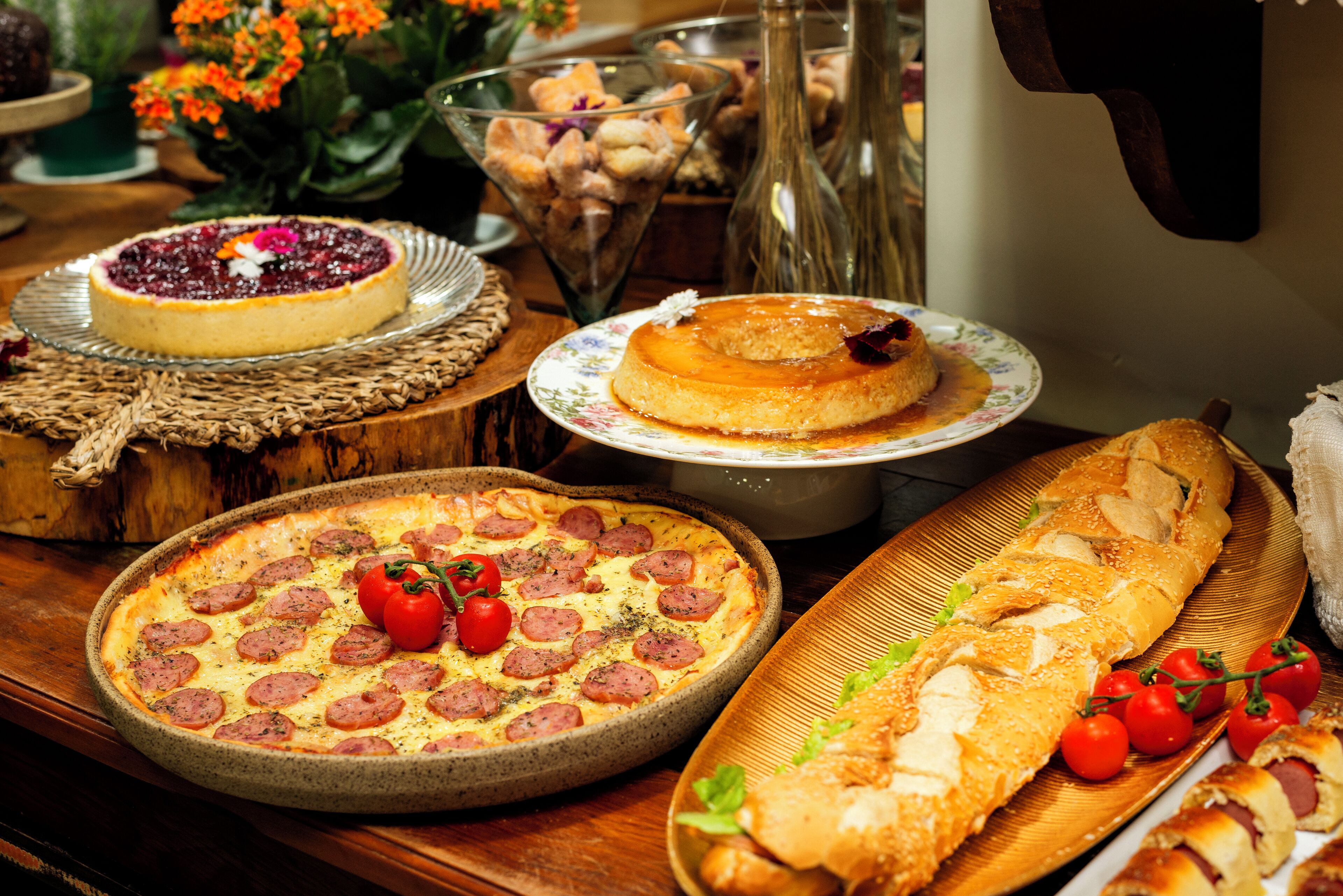 A variety of desserts including a pizza, a cheesecake, and a bread roll, displayed on a wooden table.