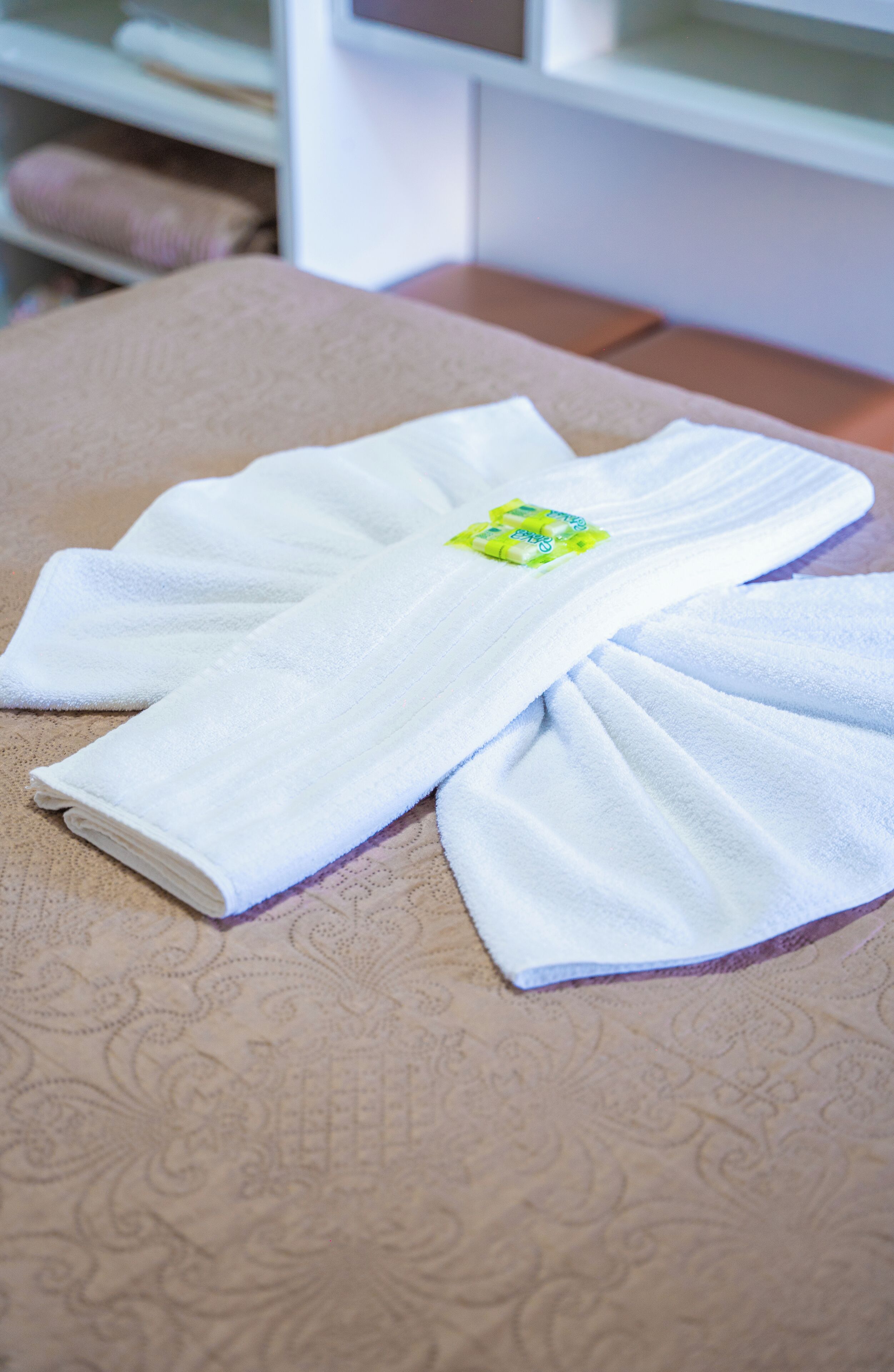 Una toalla blanca doblada con un emblema verde y amarillo sobre una superficie beige estampada.