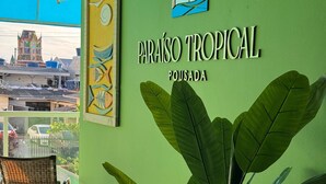 A green wall with the text "Paraíso Tropical Pousada" and a large potted plant. There are two wicker chairs in front. - Pousada Paraíso Tropical (Penha)