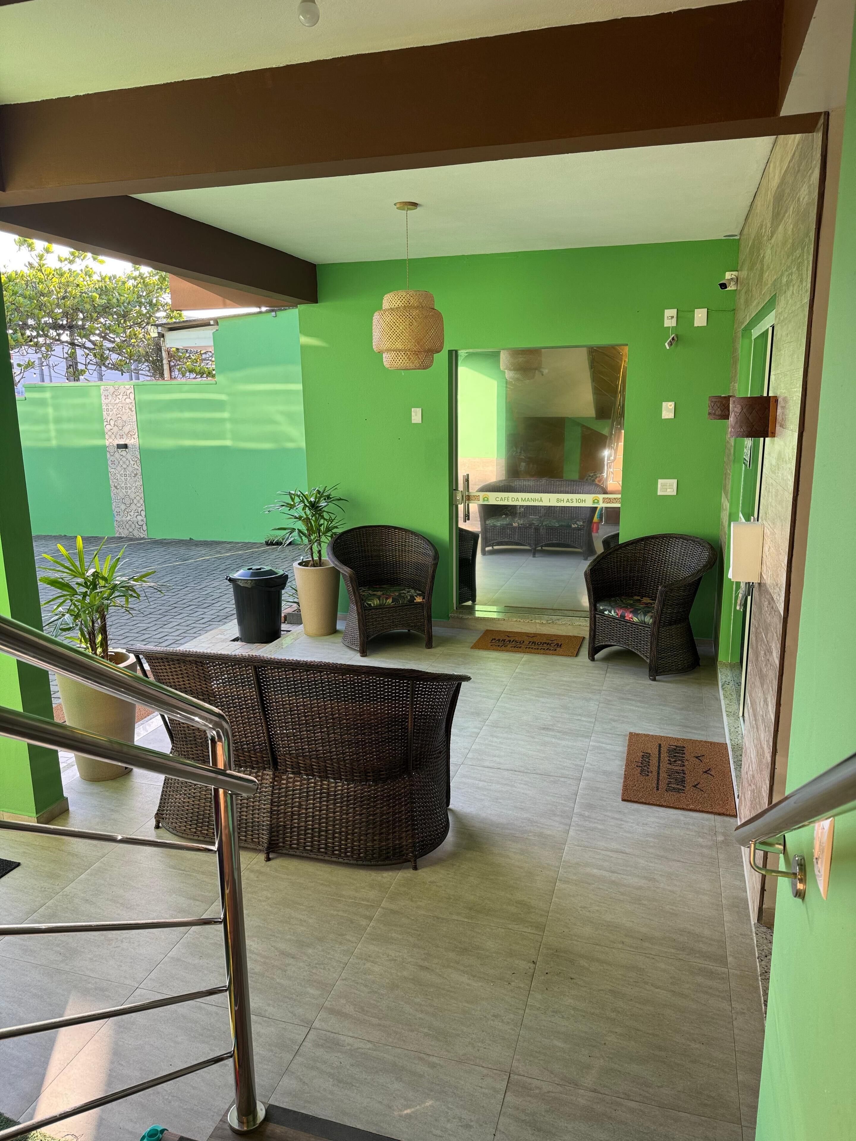 Un espace intérieur aux murs verts, aménagé avec des meubles en osier, un escalier et une porte donnant sur une autre pièce.