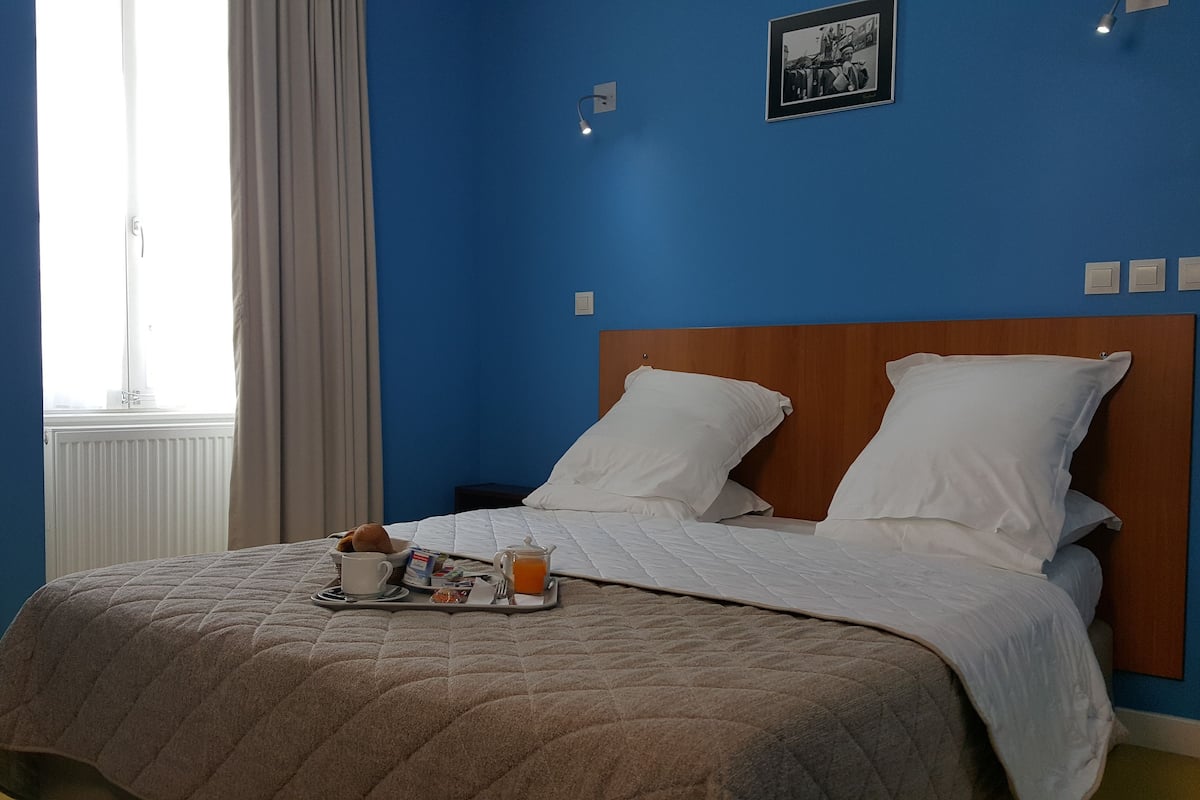 A hotel room with a bed, a tray with breakfast items, a suitcase, and a window with curtains.
