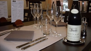 Una mesa de comedor dispuesta con copas de vino, una botella de vino Santenay y un menú.
