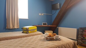 A room with two beds, a suitcase, a table with a teapot, a cup, and a basket of bread.