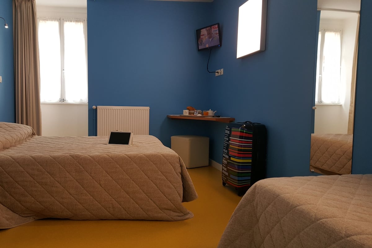 A hotel room with two beds, a desk, a chair, a TV, and a window with curtains.