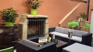 Un patio al aire libre con mobiliario de mimbre, una chimenea de piedra y plantas en macetas.