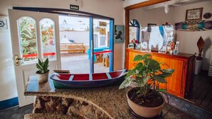 A reception area with a wooden counter, potted plants, and a view through a glass door leading outside. - Pousada Rafimar (Ilhabela)