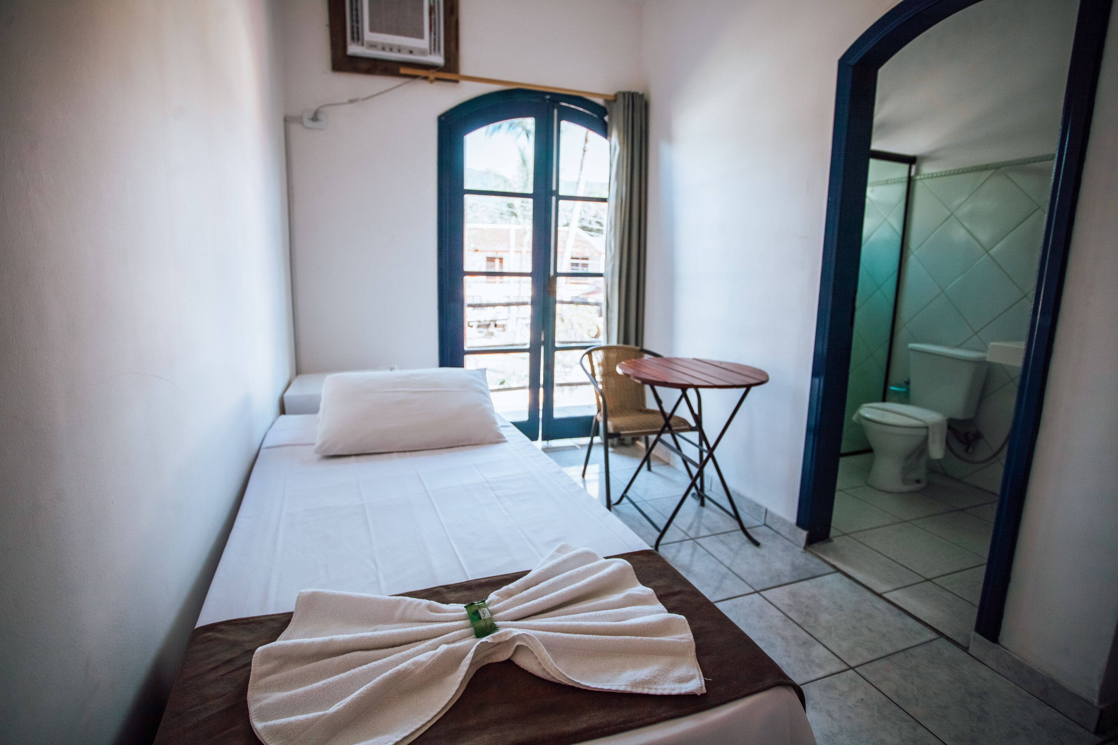 A small, clean room with a bed, a small table, and a view of the outside through a window.