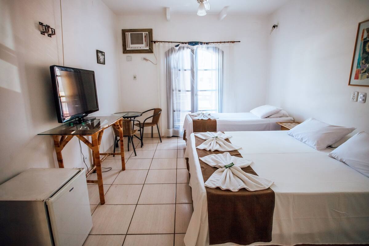 A hotel room with a bed, a desk with a television, a chair, and a small refrigerator.
