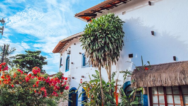 A white building with a red-tiled roof, surrounded by lush greenery and red flowers. - Pousada Rafimar (Ilhabela)