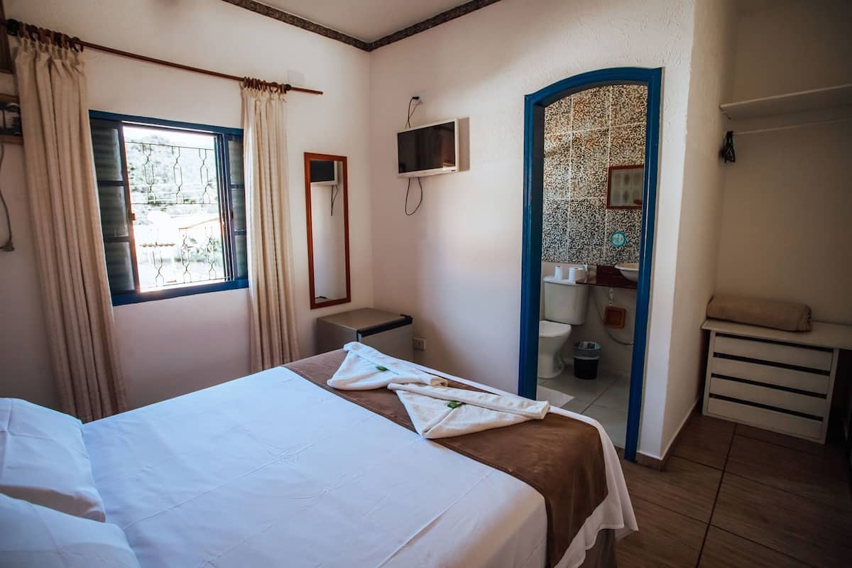 A hotel room with a bed, a TV, a bathroom, and a view of the outside.