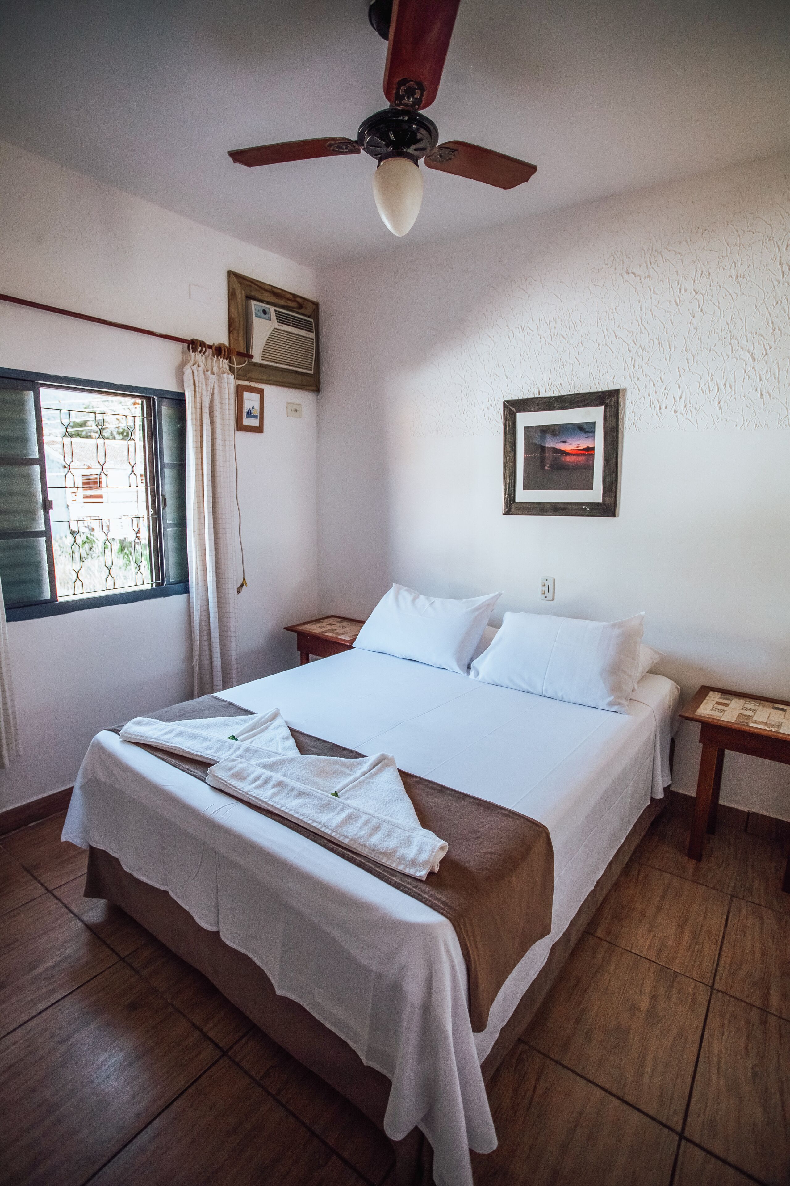 A neatly made bed with white linens, a wooden headboard, and a ceiling fan.