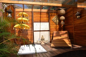 Een houten kamer met een meditatiebeeld, een glazen tafel en hangende lantaarns.