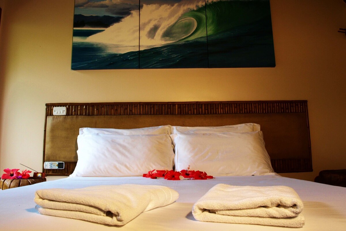 Een hotelkamer met een groot bed, twee kussens, een hoofdbord en een schilderij van een golf aan de muur.