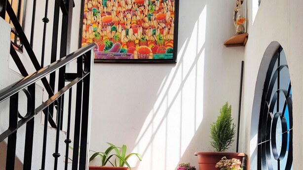 Una escalera con barandilla negra, un cuadro colorido en la pared y plantas en macetas en la plataforma.
