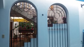 Una casa con fachada blanca, una escalera de madera y un portón de metal con un diseño circular.