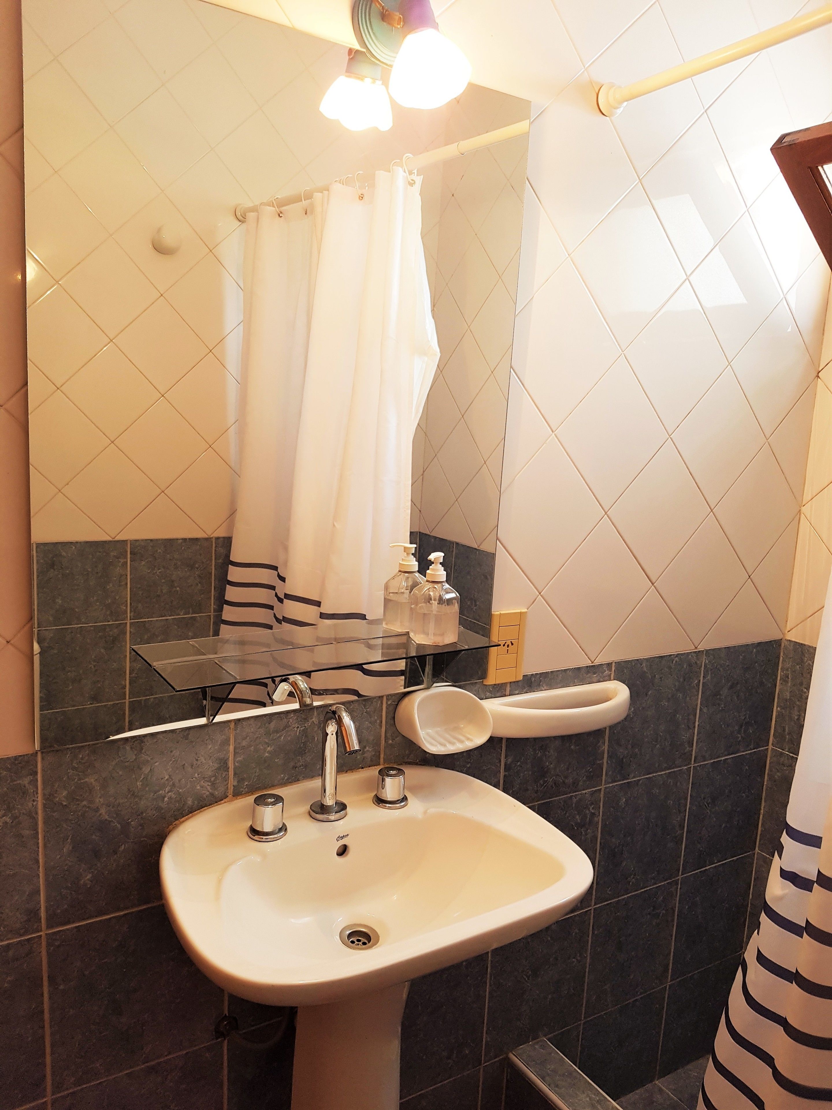 Ein Badezimmer mit einem weißen Waschbecken, einem Spiegel, einer Duschvorhang und einer Glasdusche.