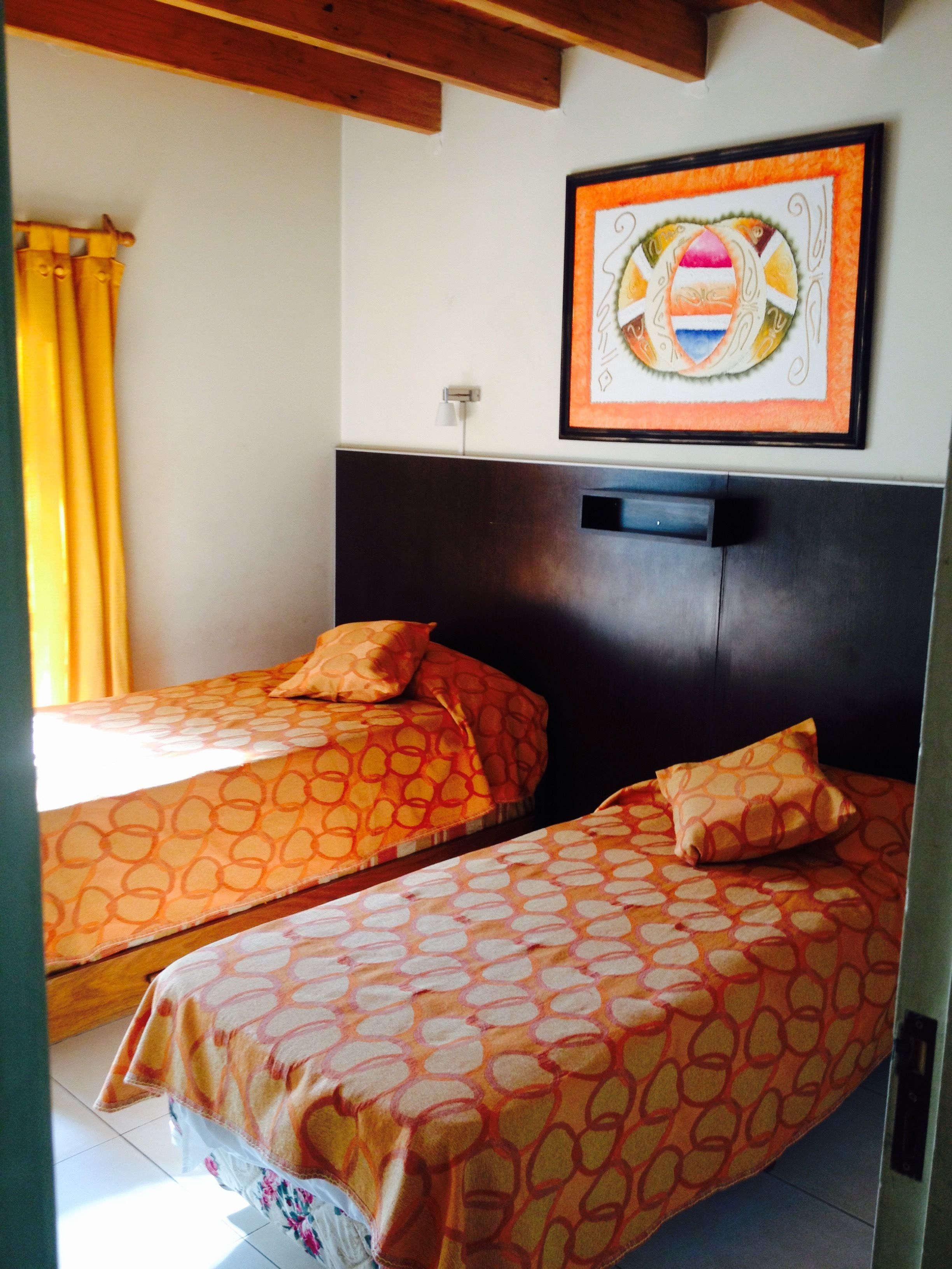 A room with two single beds, each with patterned bedding, a dark headboard, and a framed artwork above.