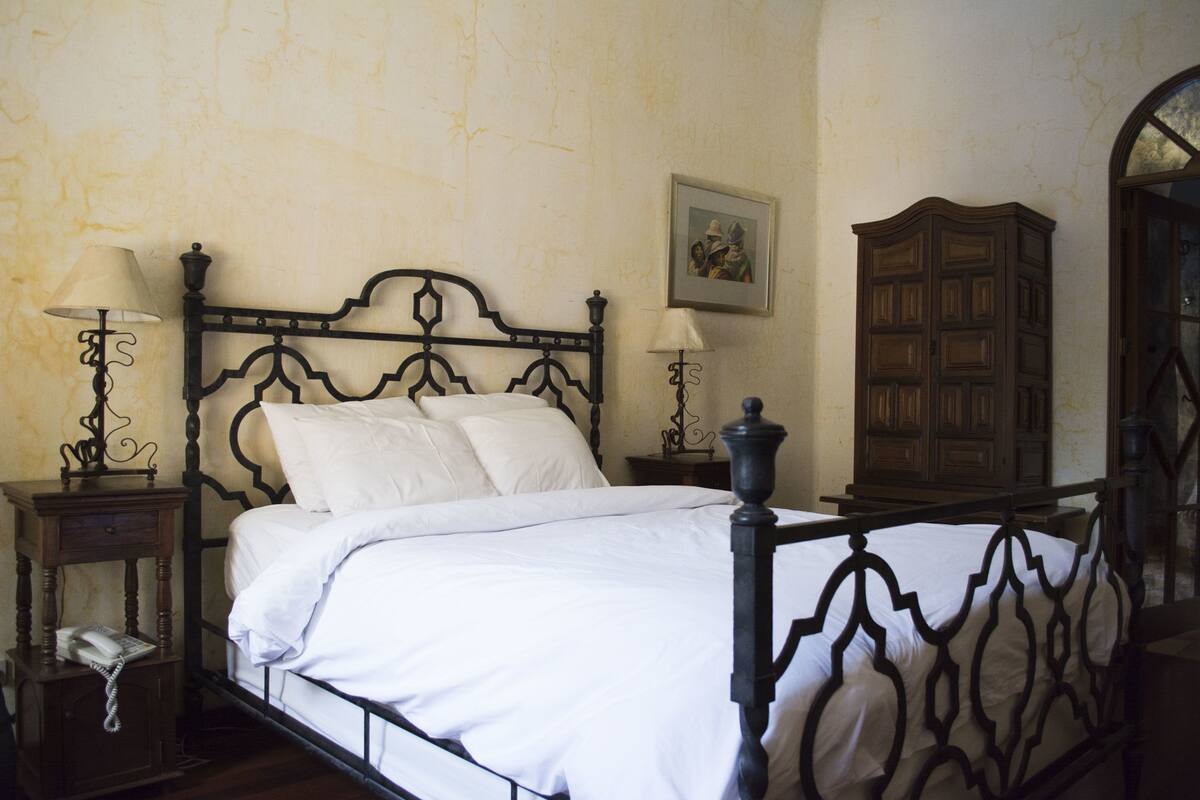 Un dormitorio con cama con dosel, dos mesitas de noche con lámparas, un armario de madera y un cuadro en la pared.