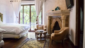 A bedroom with a bed, a chair, a small table, a fireplace, and a TV. - Posada de Los Leones (Antigua Guatemala)