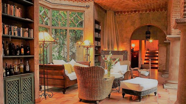 A cozy room with a fireplace, wicker furniture, and bookshelves. - Posada de Los Leones (Antigua Guatemala)
