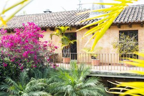 A building with a tiled roof and a balcony with potted plants. - Posada de Los Leones (Antigua Guatemala)
