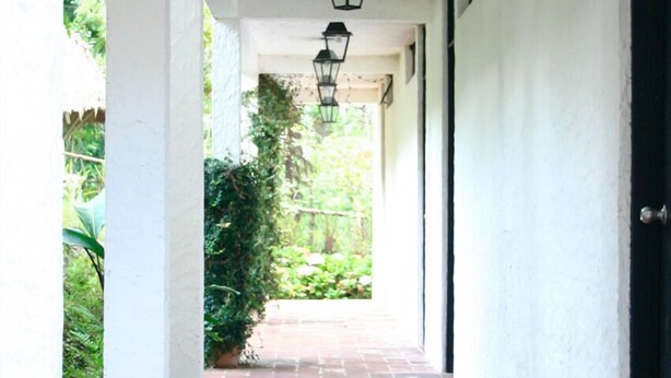 A covered walkway with a brick floor, white walls, and black lantern-style lighting fixtures. - Hotel Posada Montaña del Quetzal (Salama)