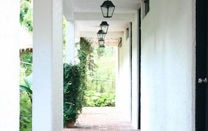 A covered walkway with a brick floor, white walls, and black lantern-style lighting fixtures. - Hotel Posada Montaña del Quetzal (Salama)