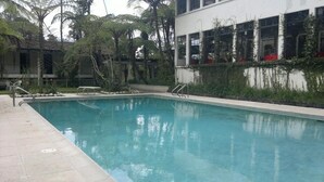 A swimming pool with a tiled deck, surrounded by greenery and a building with large windows. - Hotel Posada Montaña del Quetzal (Salama)