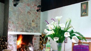 A room with a stone fireplace, a table with a vase of flowers, and a chair with a colorful cushion. - Hotel Posada Montaña del Quetzal (Salama)