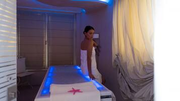 A spa room with a massage table, a starfish towel, and a window with curtains.