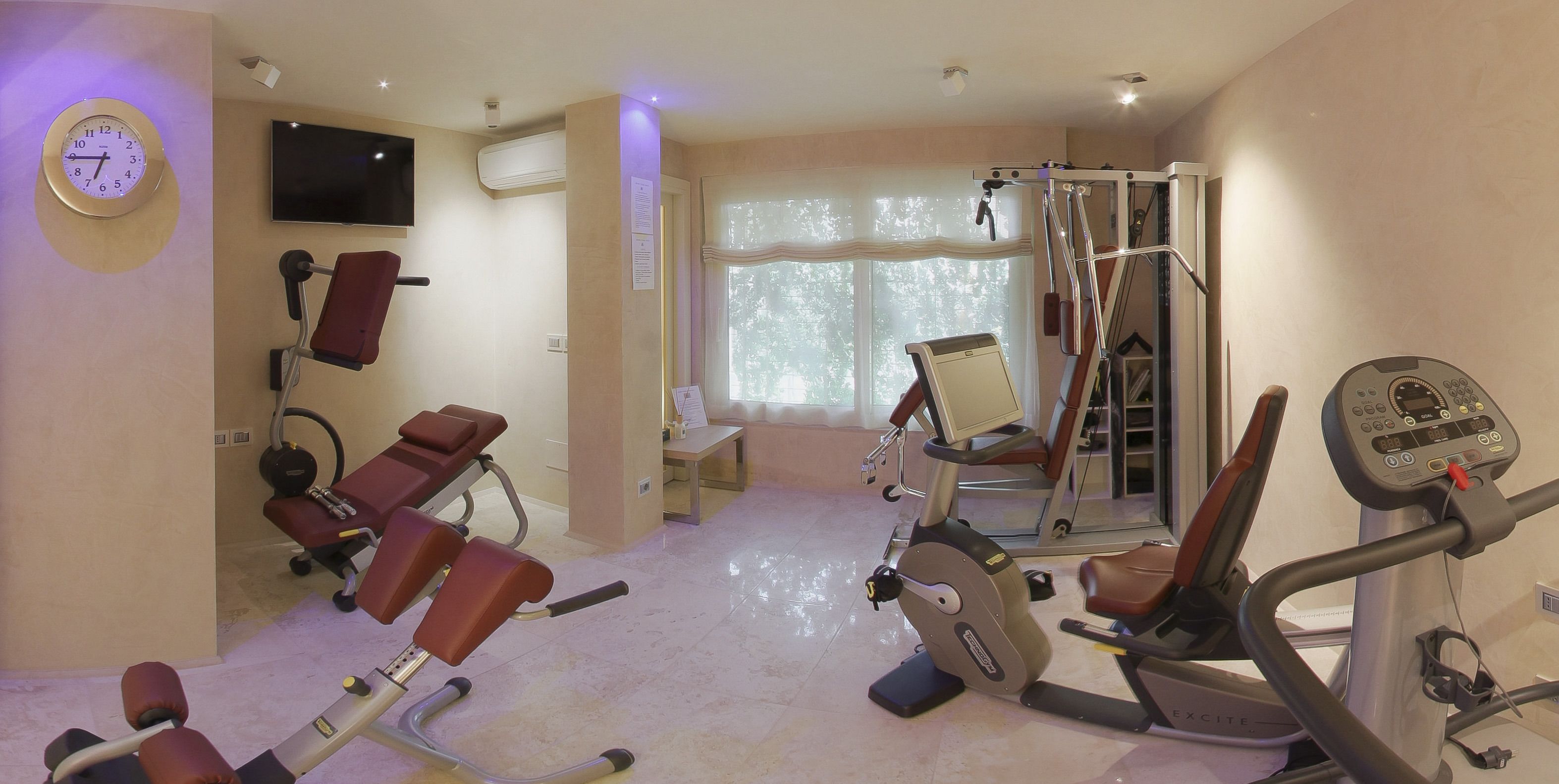 A gym with exercise equipment, a TV, and a clock on the wall.