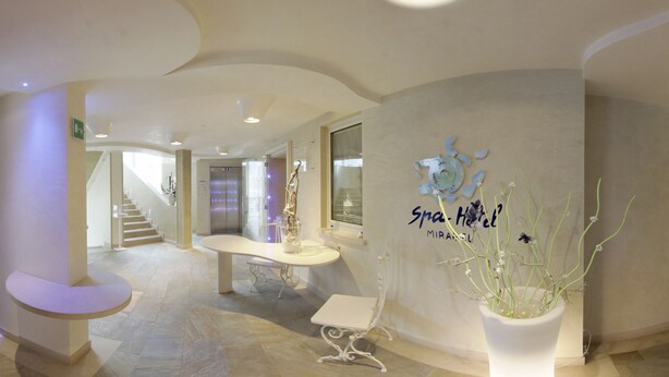 A modern hotel lobby with a reception desk, a staircase, and a potted plant. - Residence Spa Mirabel (Grado)