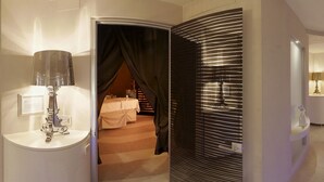 A hotel room with a bed, a bathroom with a mirror and sink, and a view of a staircase. - Residence Spa Mirabel (Grado)