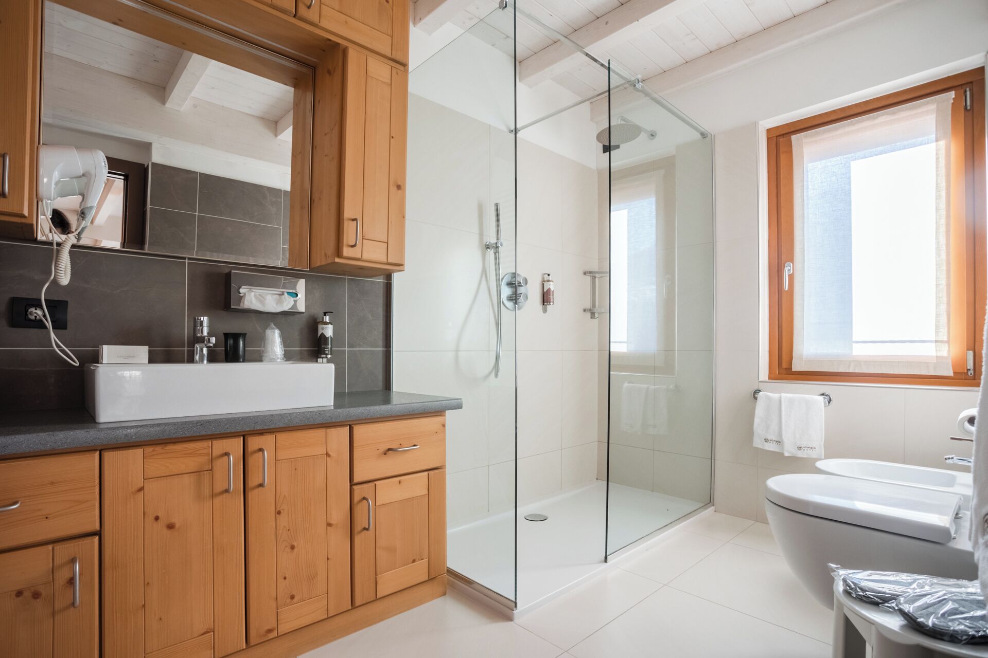 Un baño moderno con cabina de ducha de vidrio, un lavamanos blanco y armarios de madera.