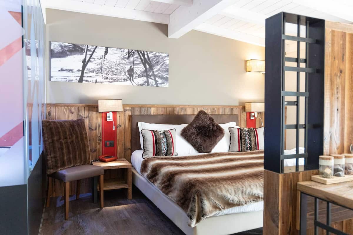 A bedroom with a bed, a chair, a nightstand, a lamp, and a wall-mounted picture.
