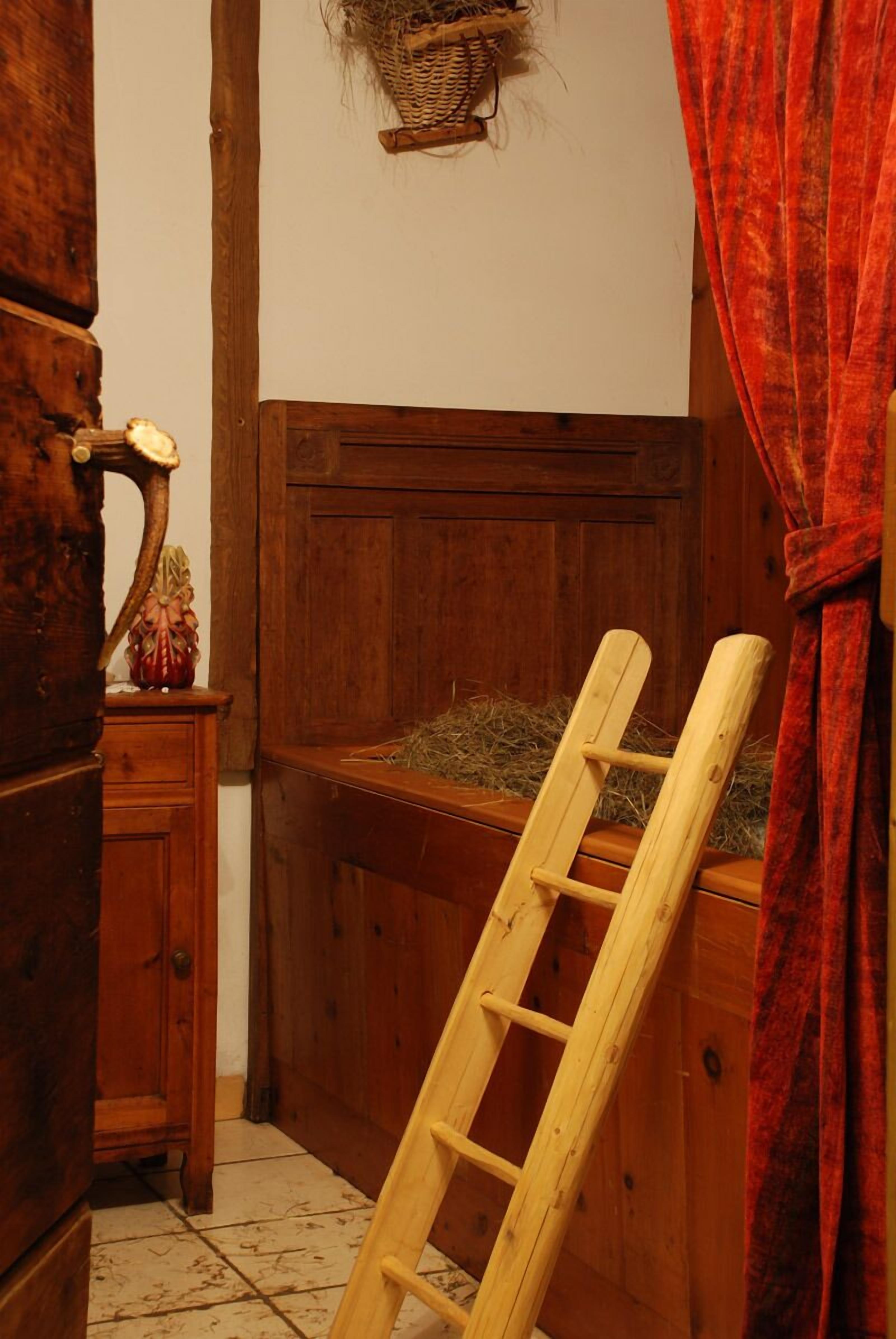 A wooden room with a ladder leaning against a wall, a wooden cabinet, and a basket on the wall.