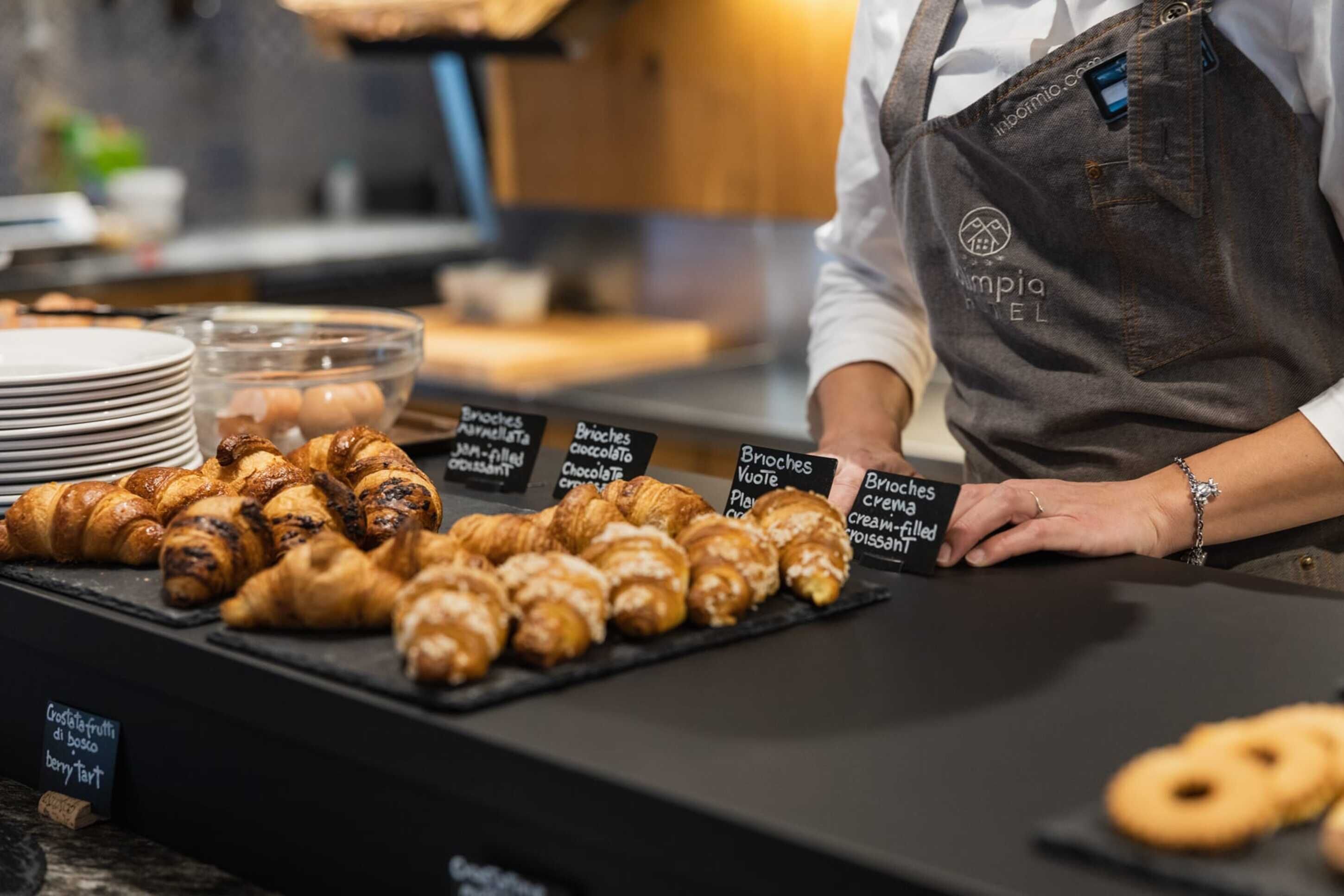 A bakery counter with various types of pastries and a person wearing an apron.
