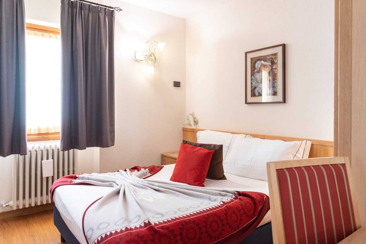 A hotel room with a bed, a nightstand, a lamp, a framed picture, and a window with curtains.
