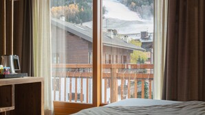 A hotel room with a large window overlooking a snowy mountain and a forest. - Olimpia Hotel (Bormio)