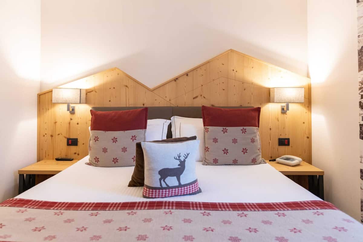 A bedroom with a wooden headboard, two bedside tables, a bed with a checkered bedspread, and decorative pillows including one with a deer silhouette.