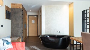 A modern bathroom with a freestanding bathtub, wooden flooring, and a wooden bench. - Olimpia Hotel (Bormio)