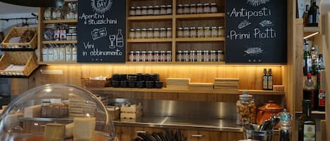 Un comptoir de restaurant où sont exposés des bocaux et des bouteilles, un tableau noir servant de menu, ainsi qu’une variété de condiments et d’ustensiles.