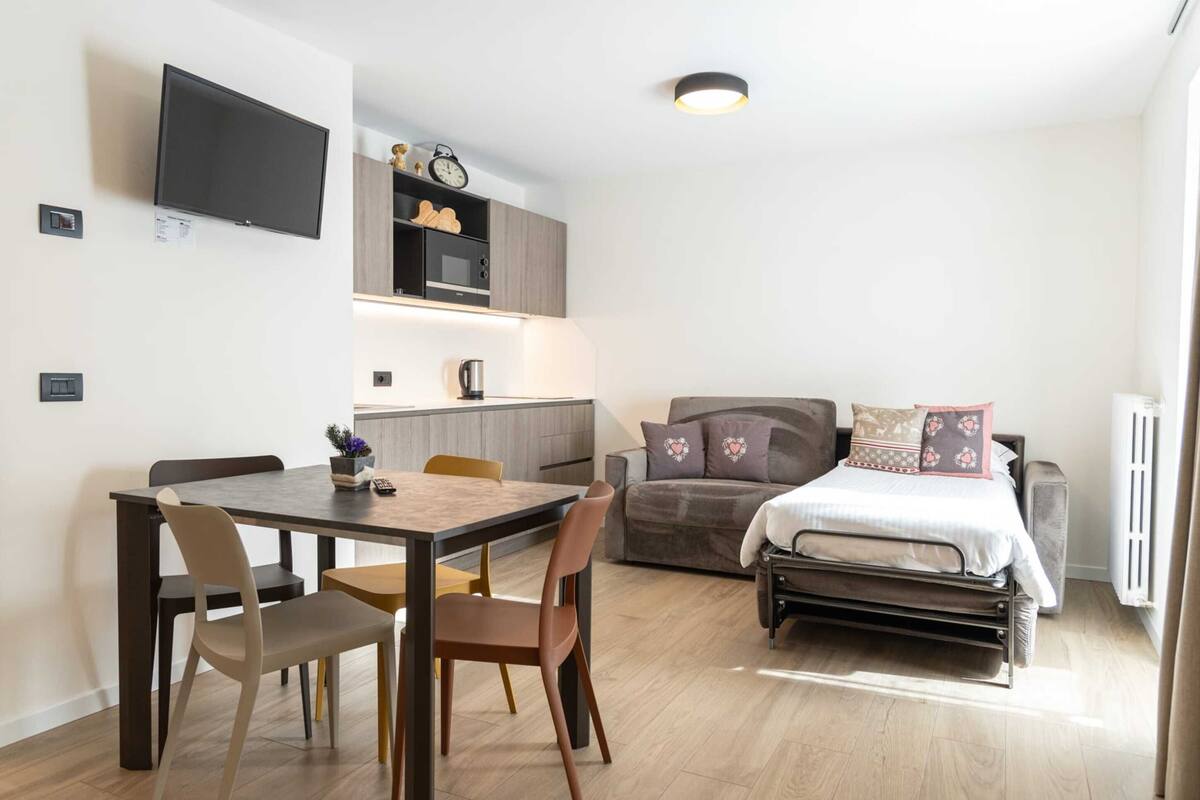 A compact living space with a dining area, kitchenette, and a bed with decorative pillows.