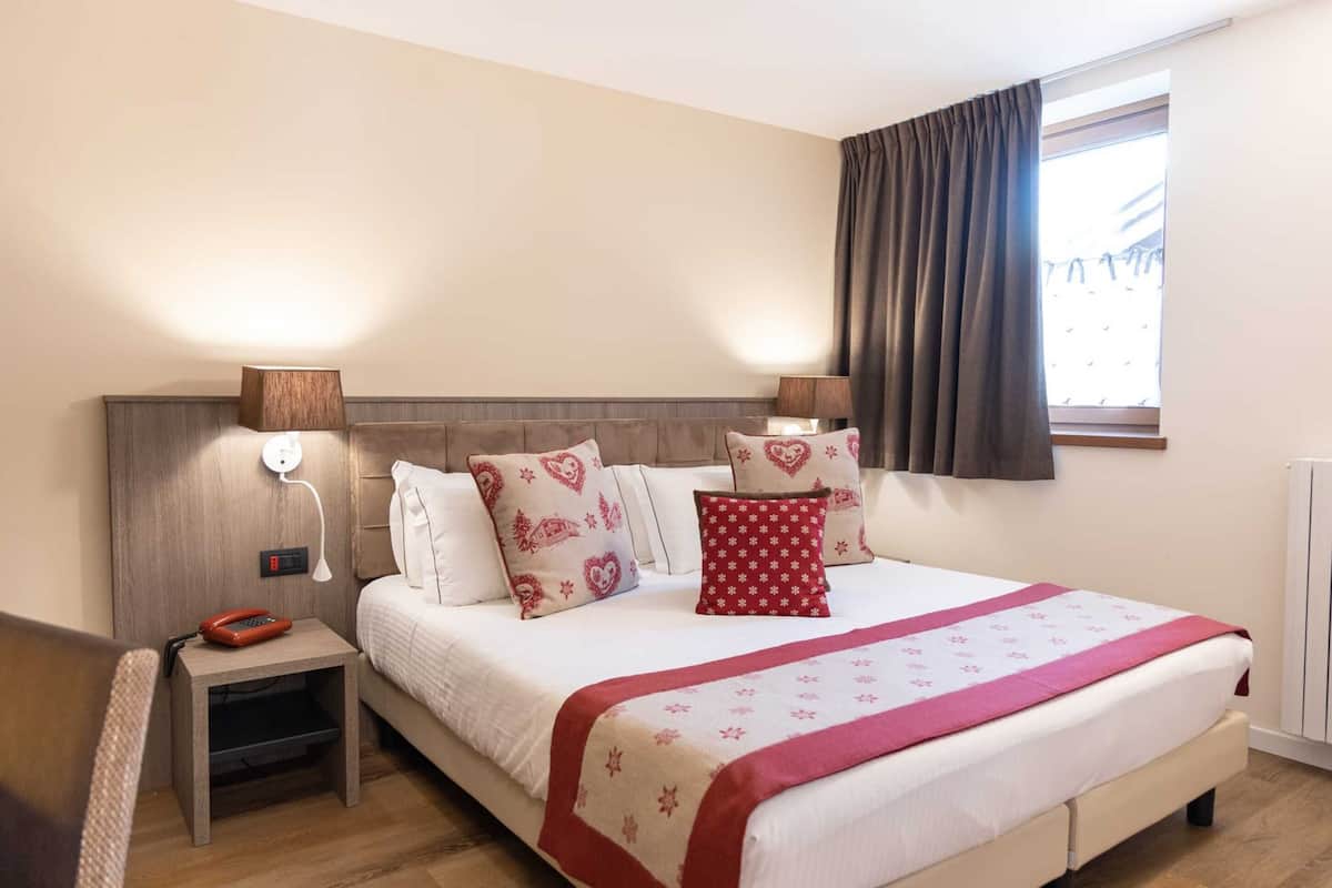 A neatly arranged bedroom with a bed, bedside lamps, a nightstand, and a window with curtains.