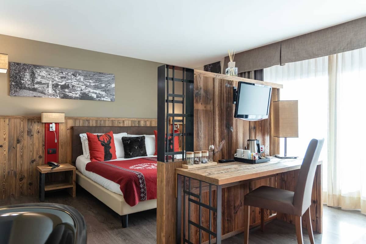 A hotel room with a bed, a desk, a TV, and a large window.
