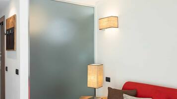 Una camera moderna con un divano rosso, un tavolino in legno, una lampada e una porta in vetro satinato.