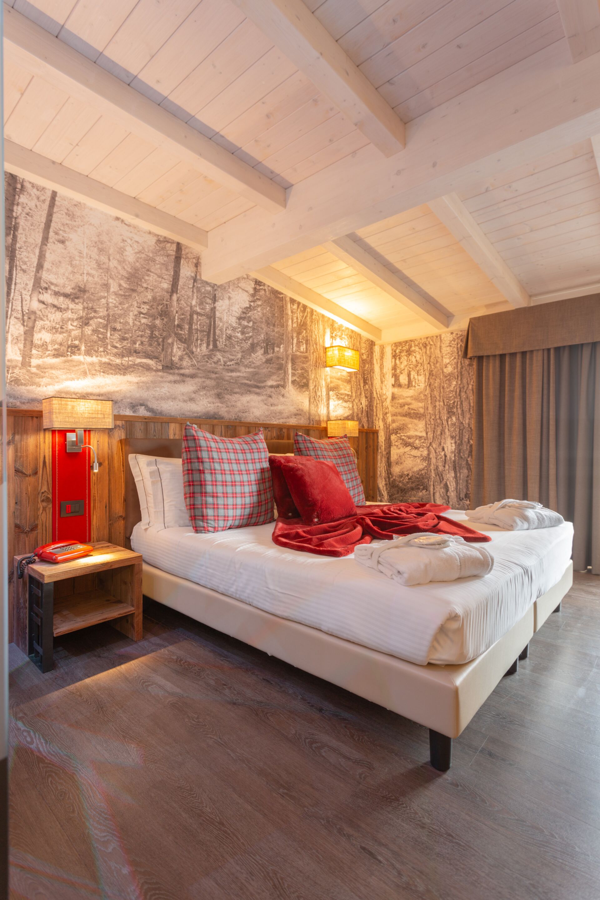 A spacious bedroom with a large bed, wooden headboard, and a forest-themed mural on the wall.