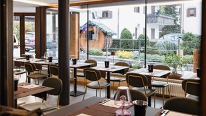 A restaurant with tables and chairs arranged for dining, large windows offering a view of the street and buildings outside. - Olimpia Hotel (Bormio)