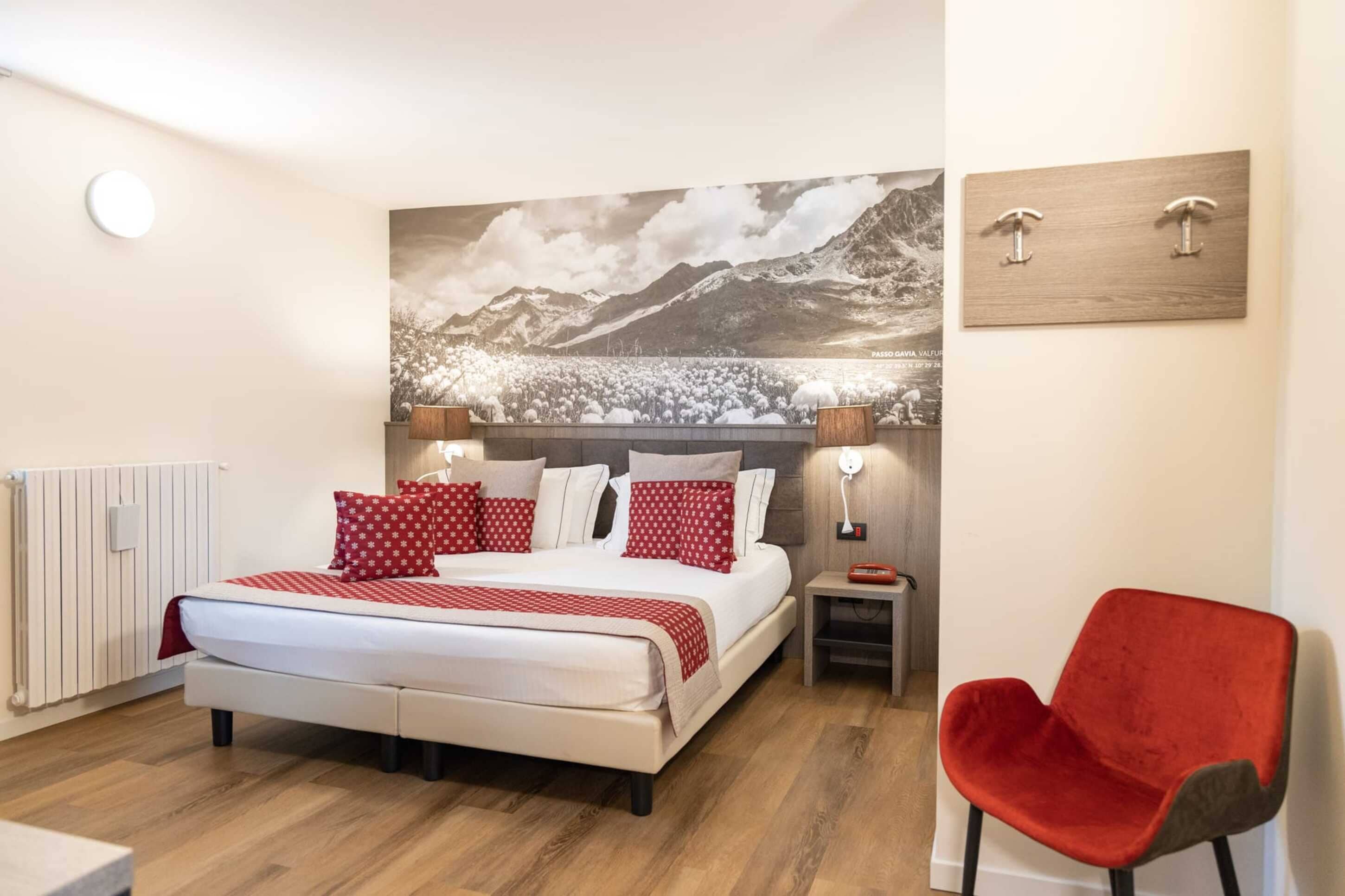 A bedroom with a bed, a red chair, a nightstand, and a wall-mounted light.