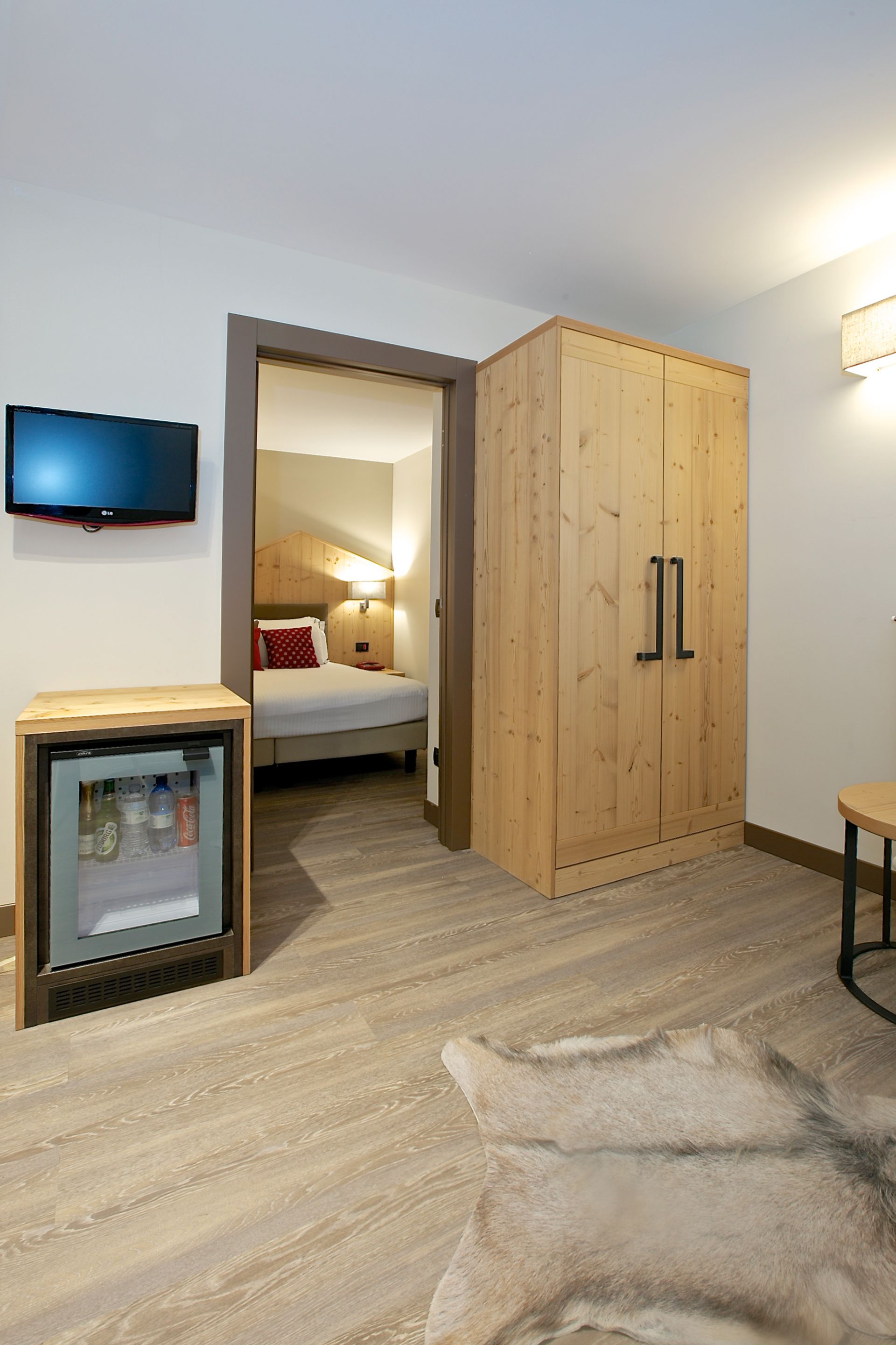 A room with a bed, a wooden wardrobe, a television, a small fridge, and a leather rug.